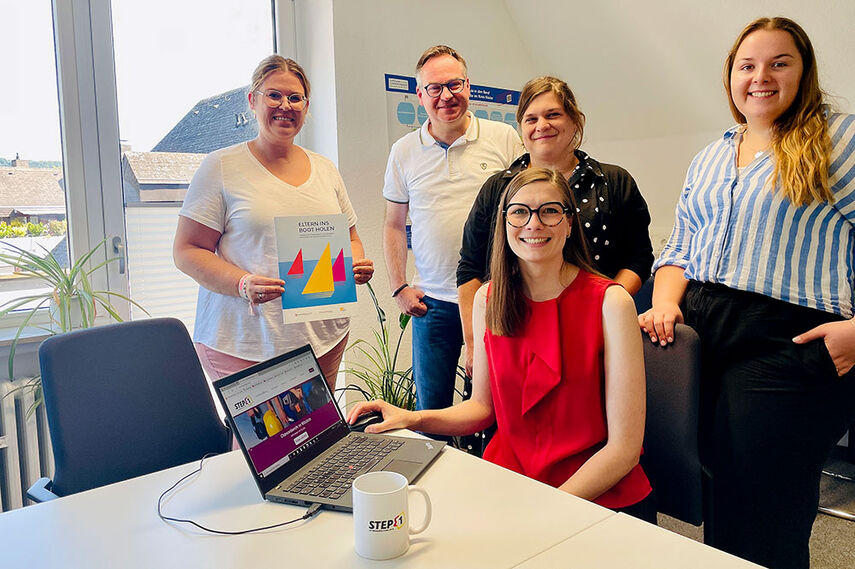 5 Personen sitzen in einem Raum vor einem Laptop